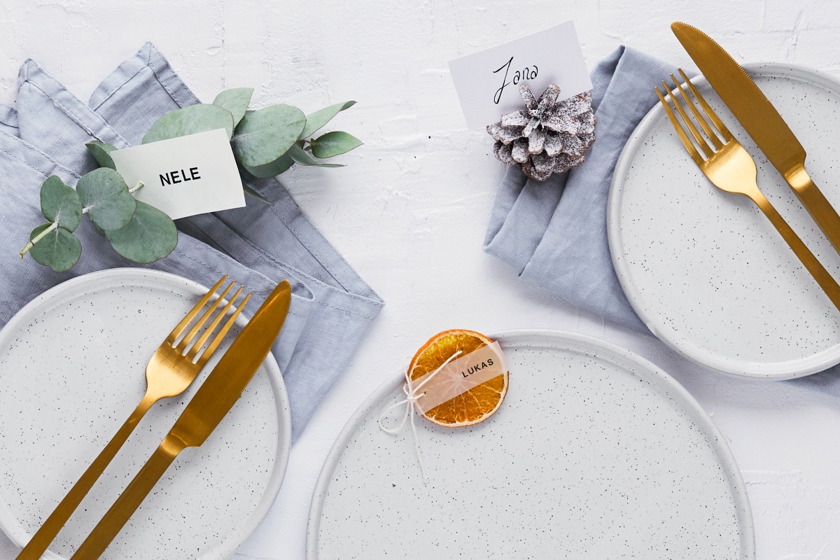 Elegant gedeckter Weihnachtstisch mit goldfarbenem Besteck, Namenskarten und getrockneten Orangenscheiben als Platzkarten.