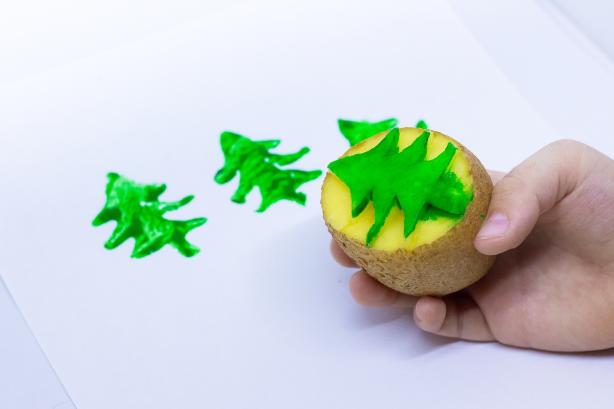 Kind stempelt grüne Tannenbäume mit einer Kartoffel auf eine Weihnachtskarte.