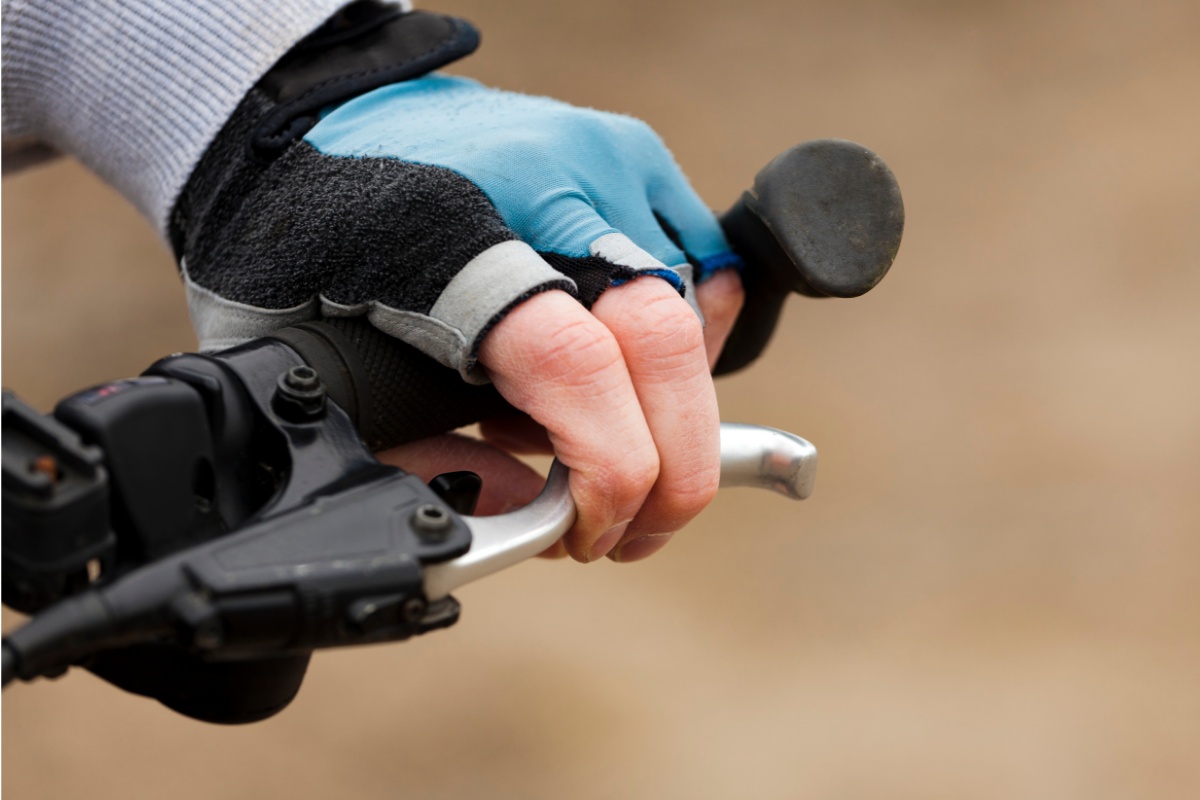 Nahaufnahme einer Hand mit Radler-Handschuhen am Griff eines Fahrradlenkers mit Barends, die Bremse ziehend.