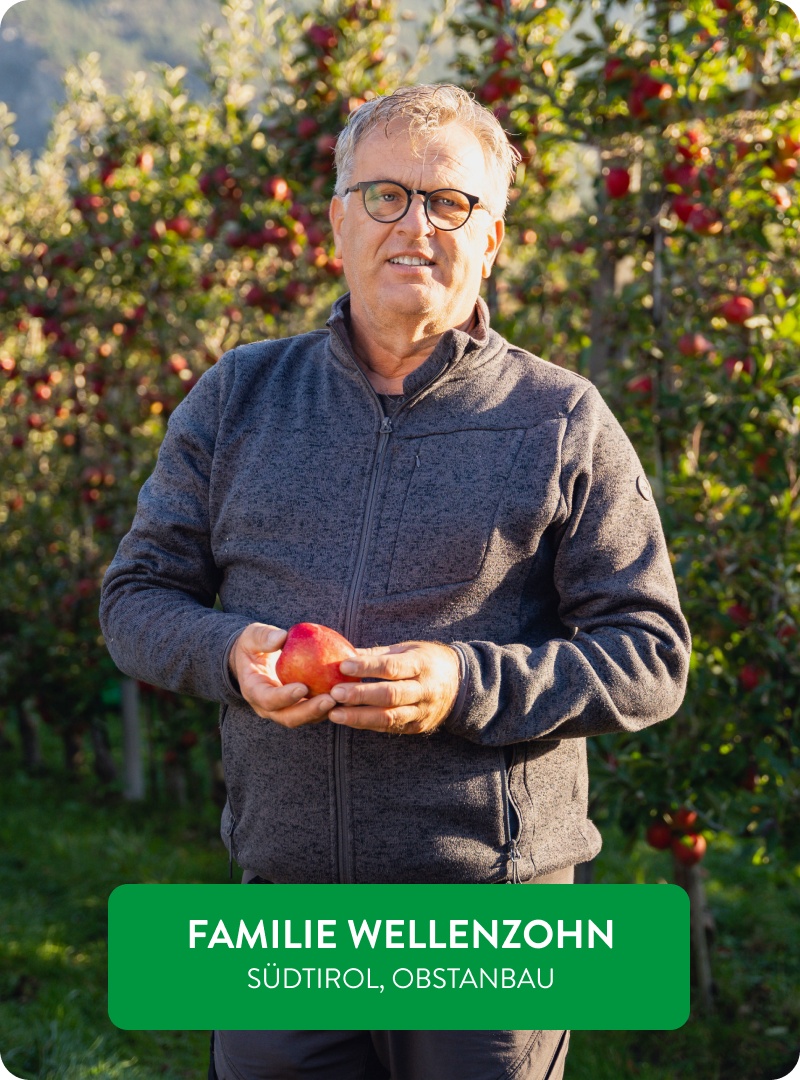 Biolandwirt Paul Wellenzohn hält einen reifen roten Apfel in einem üppigen Obstgarten