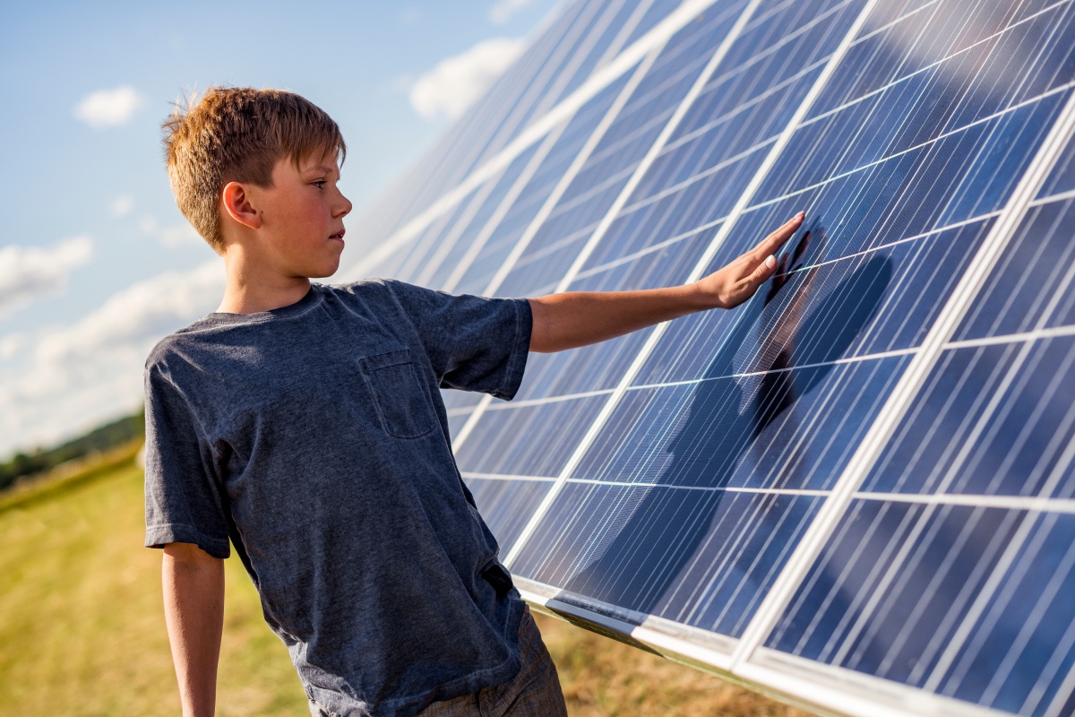 Junge im grauen T-Shirt berührt Solarpanel auf einem Feld bei sonnigem Wetter.