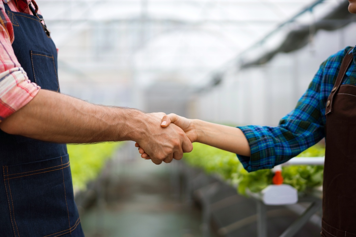 Zwei Landwirte schütteln sich die Hand im Gewächshaus.