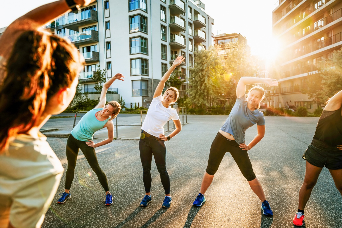 Gruppe von Frauen, die auf einem Platz in der Stadt bei Sonnenuntergang gemeinsam Dehnübungen macht.