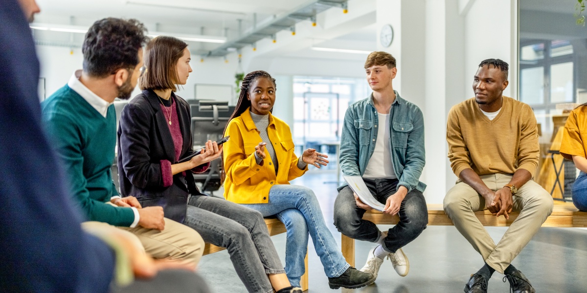 Gruppe junger Menschen sitzt in einem Kreis in einem modernen Büro und diskutiert engagiert.