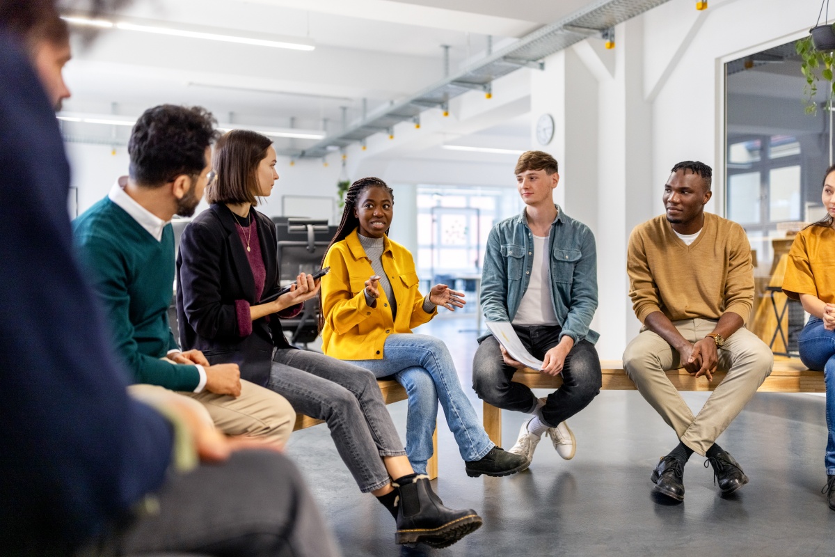Gruppe junger Menschen sitzt in einem Kreis in einem modernen Büro und diskutiert engagiert.