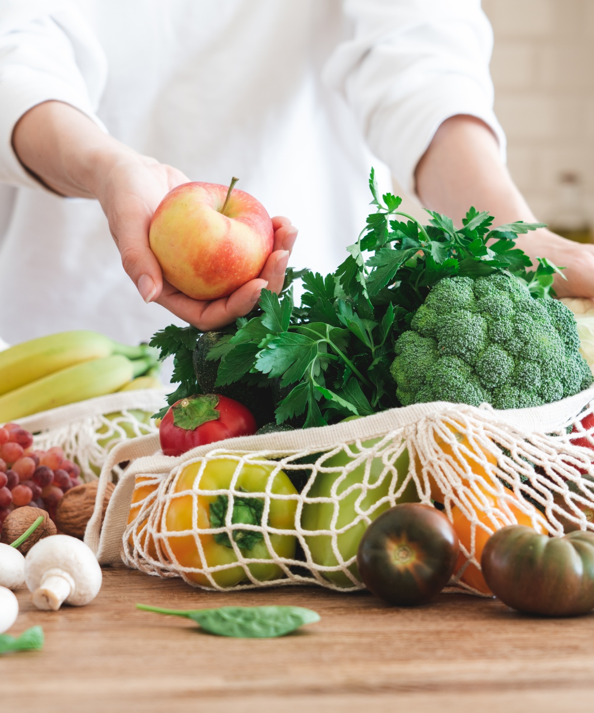 Person holt einen Apfel aus einer großen Netz-Einkaufstasche, die gefüllt ist mit viel frischem Gemüse.
