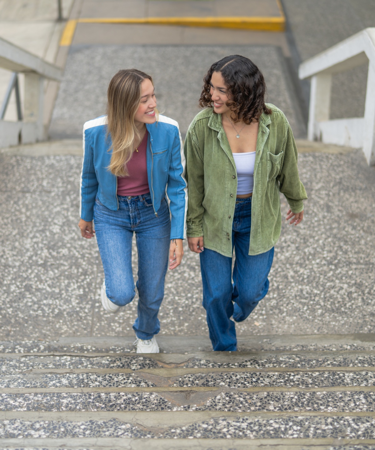 Zwei junge Frauen in lässiger Kleidung gehen lächelnd eine Treppe im Freien hinauf.