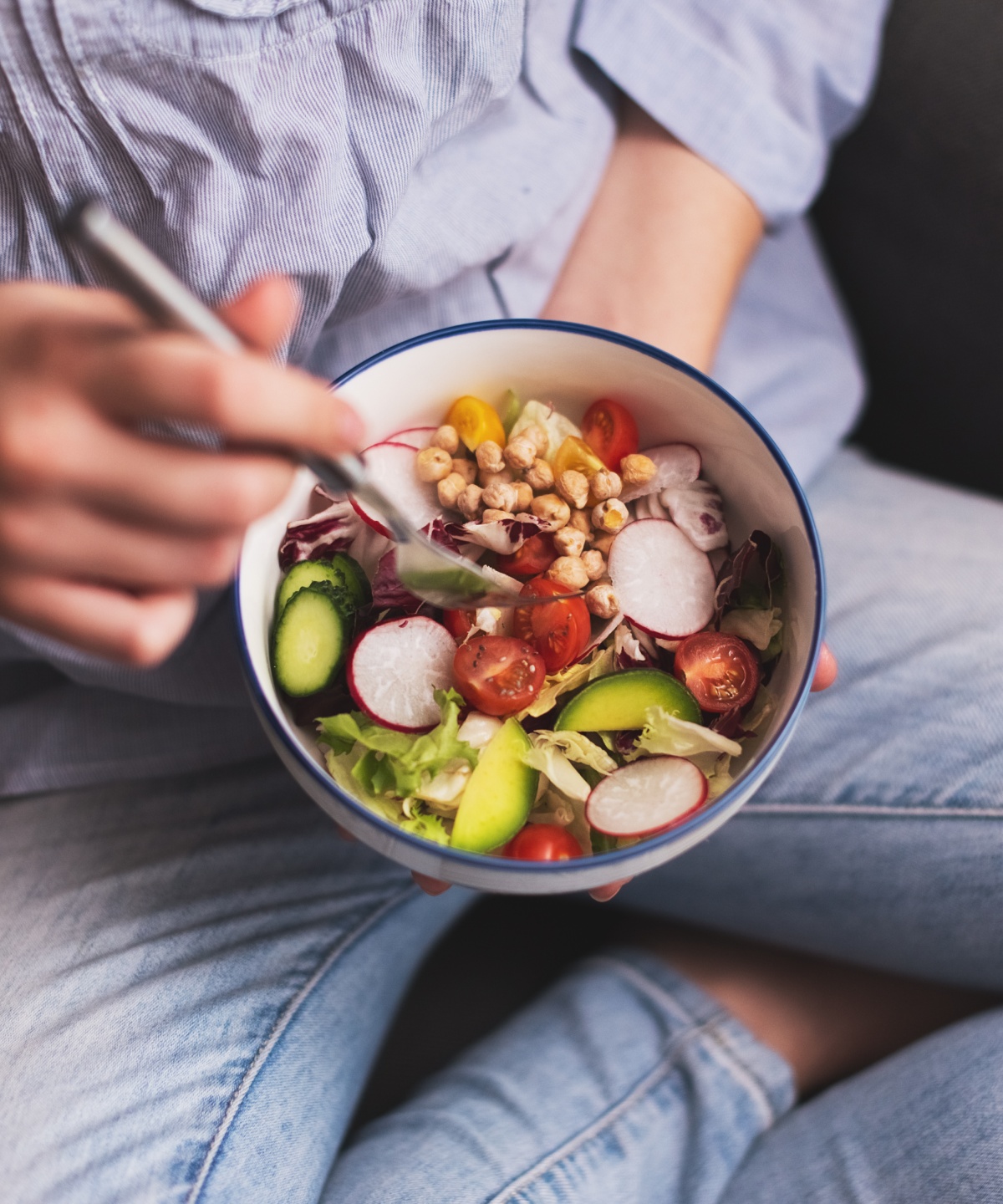 Person hält eine Schüssel mit frischem Gemüsesalat und isst mit einer Gabel.