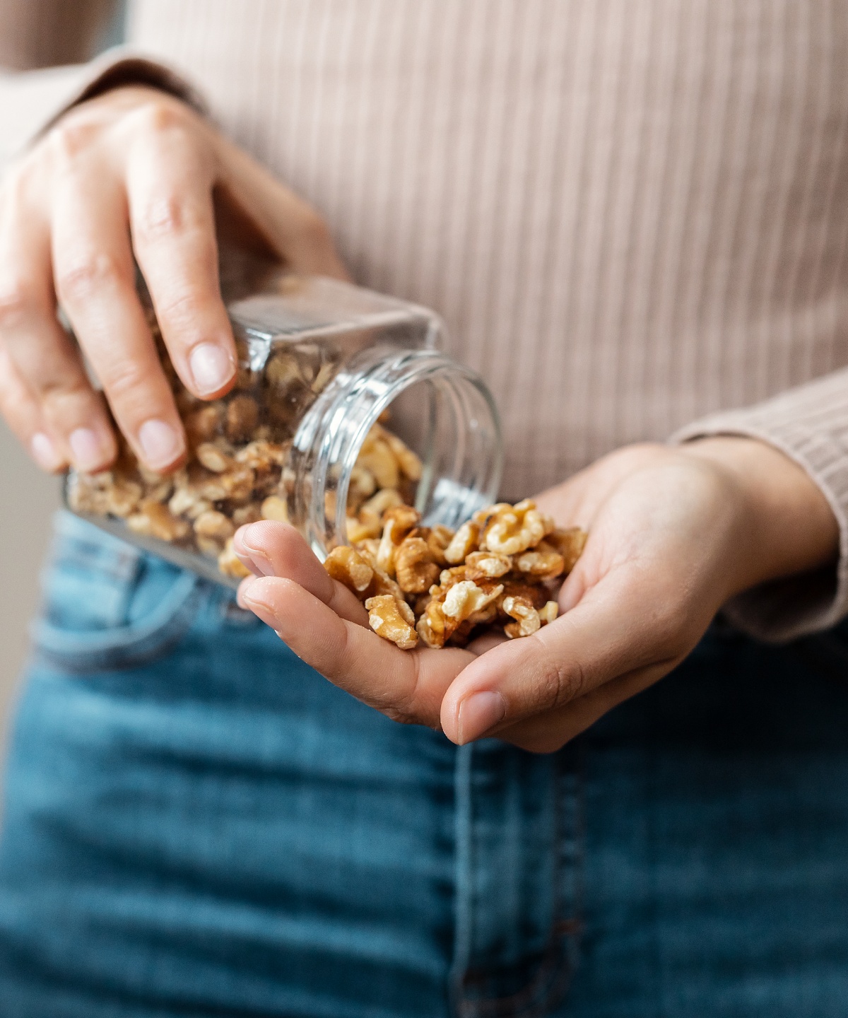 Person füllt Walnüsse aus einem Glas in die Hand.