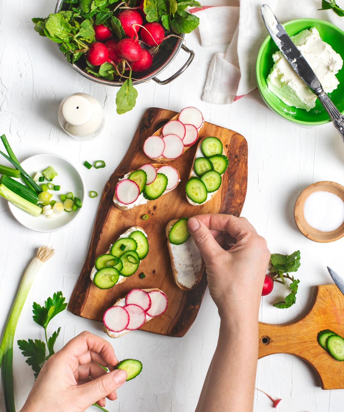 Frische Brot-Scheiben werden mit Gurken- und Radieschenscheiben auf einem Holzbrett belegt.