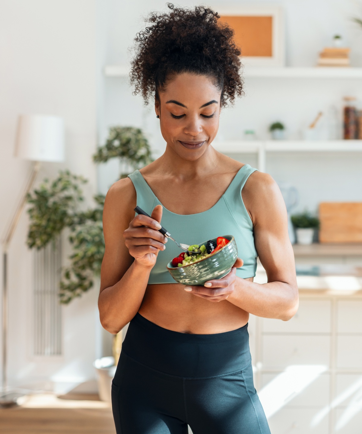 Frau in Sportkleidung isst eine selbstgemachte Bowl in einer modernen Küche nach dem Training.