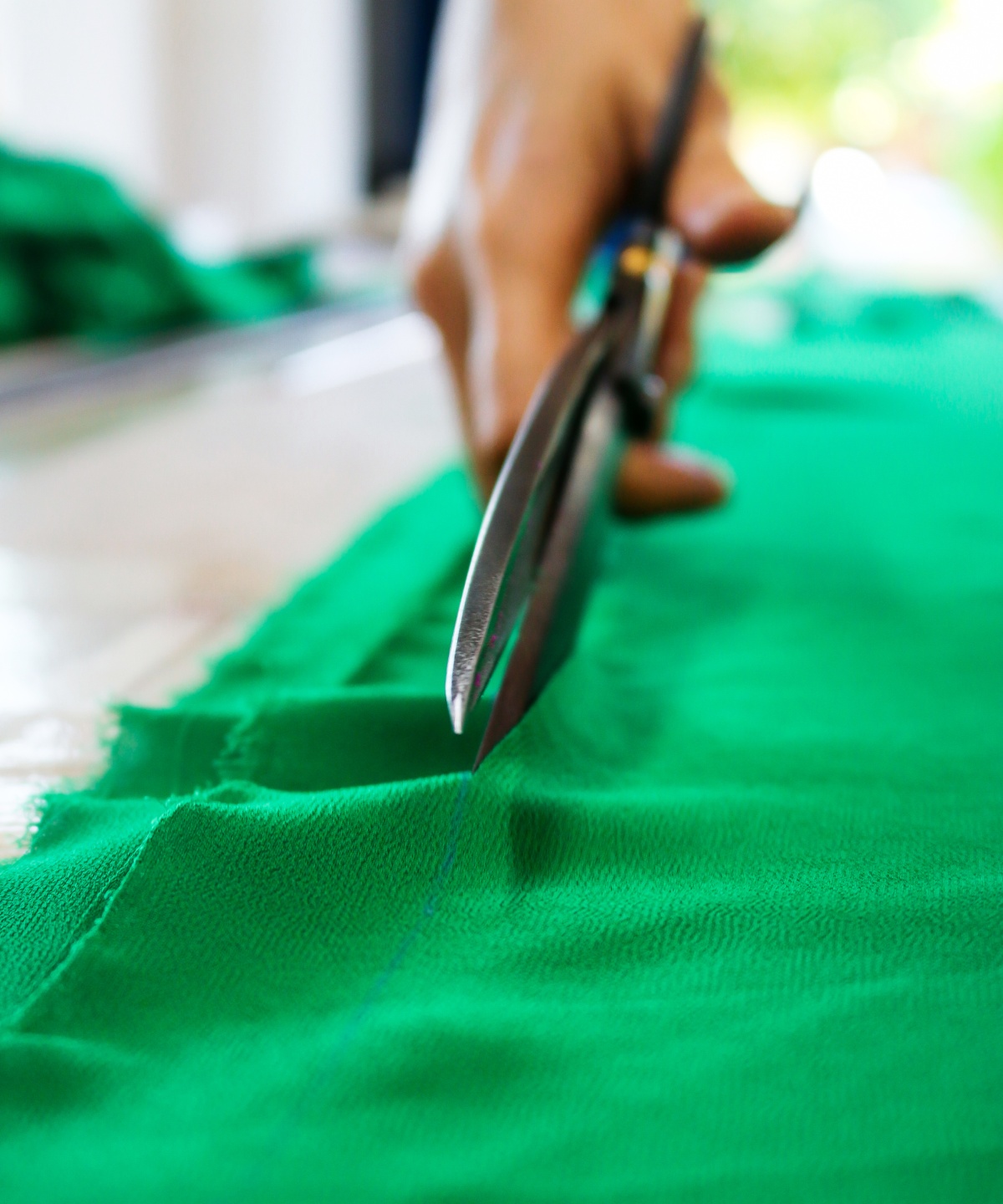 Eine Hand schneidet durch grünen Stoff.