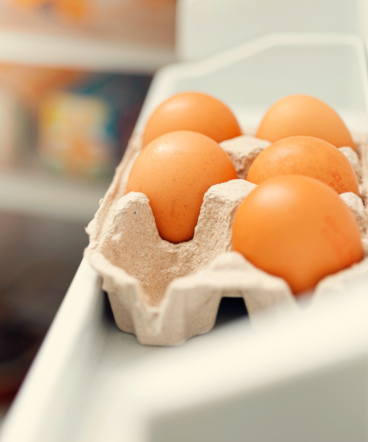 Ein Eierkarton gefüllt mit Eiern im offenen Kühlschrank.