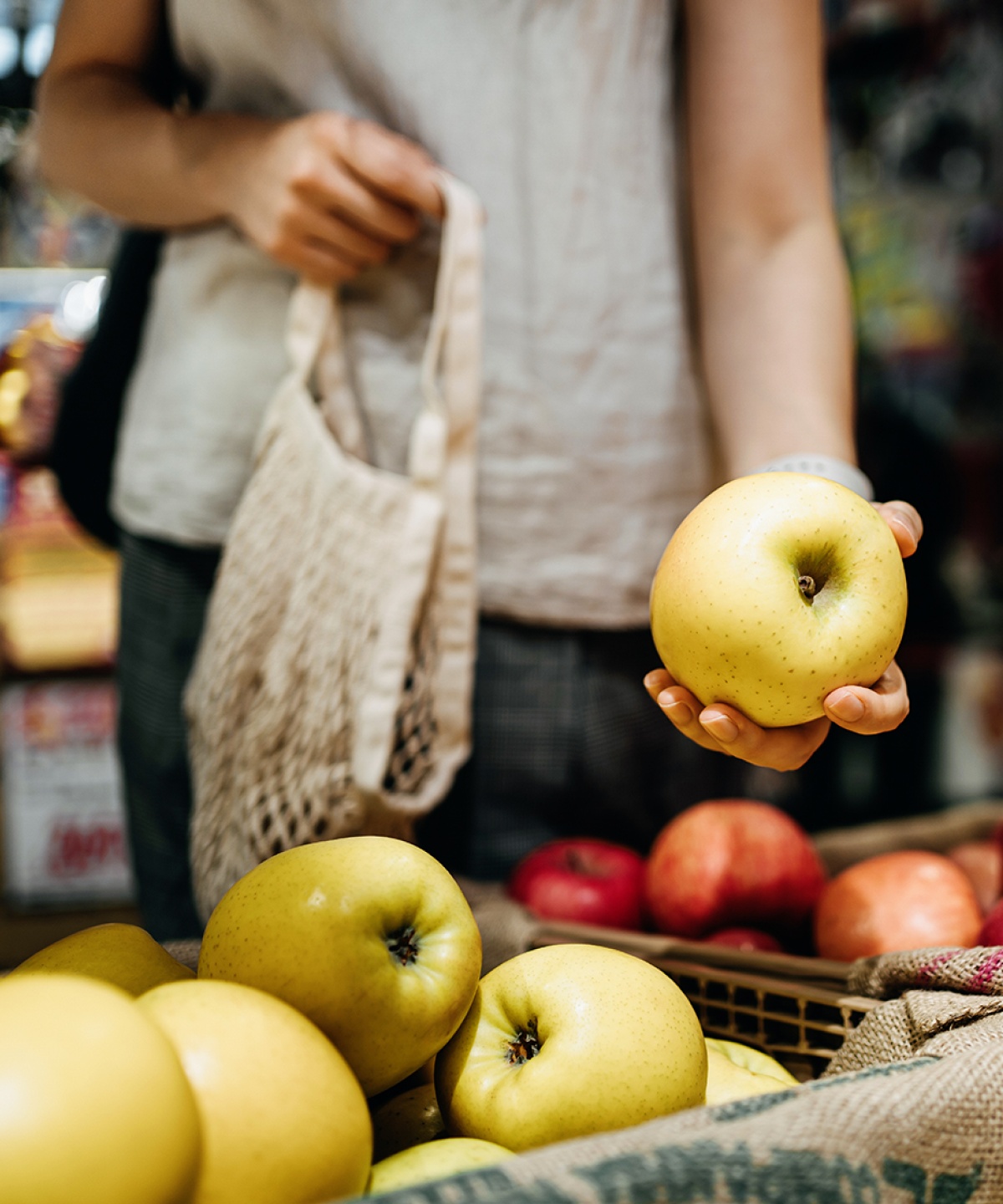 Eine Frau greift nach unverpackten Äpfeln im Geschäft.