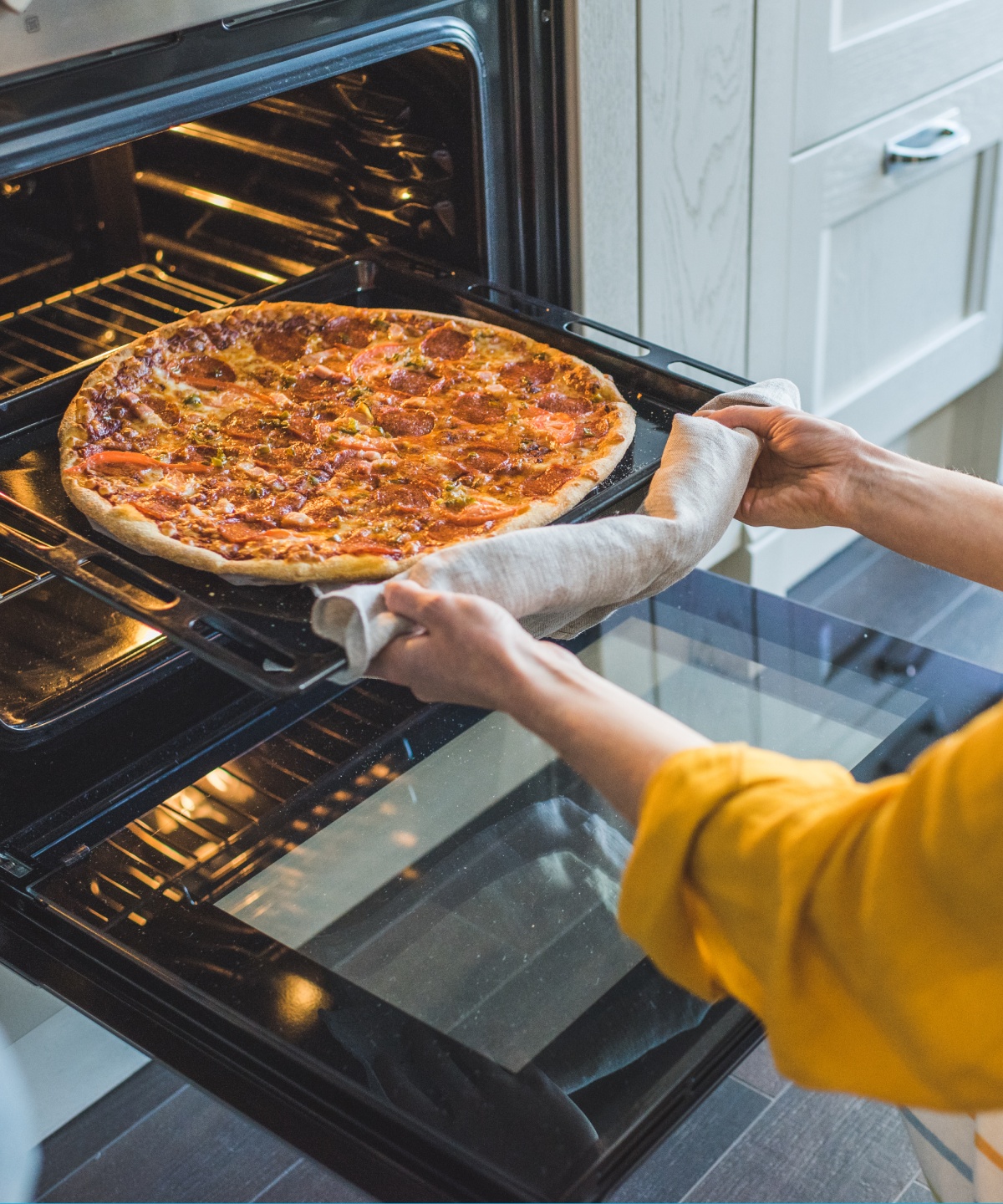 Eine fertig gebackene Pizza wird von einer Frau aus dem Ofen geholt.