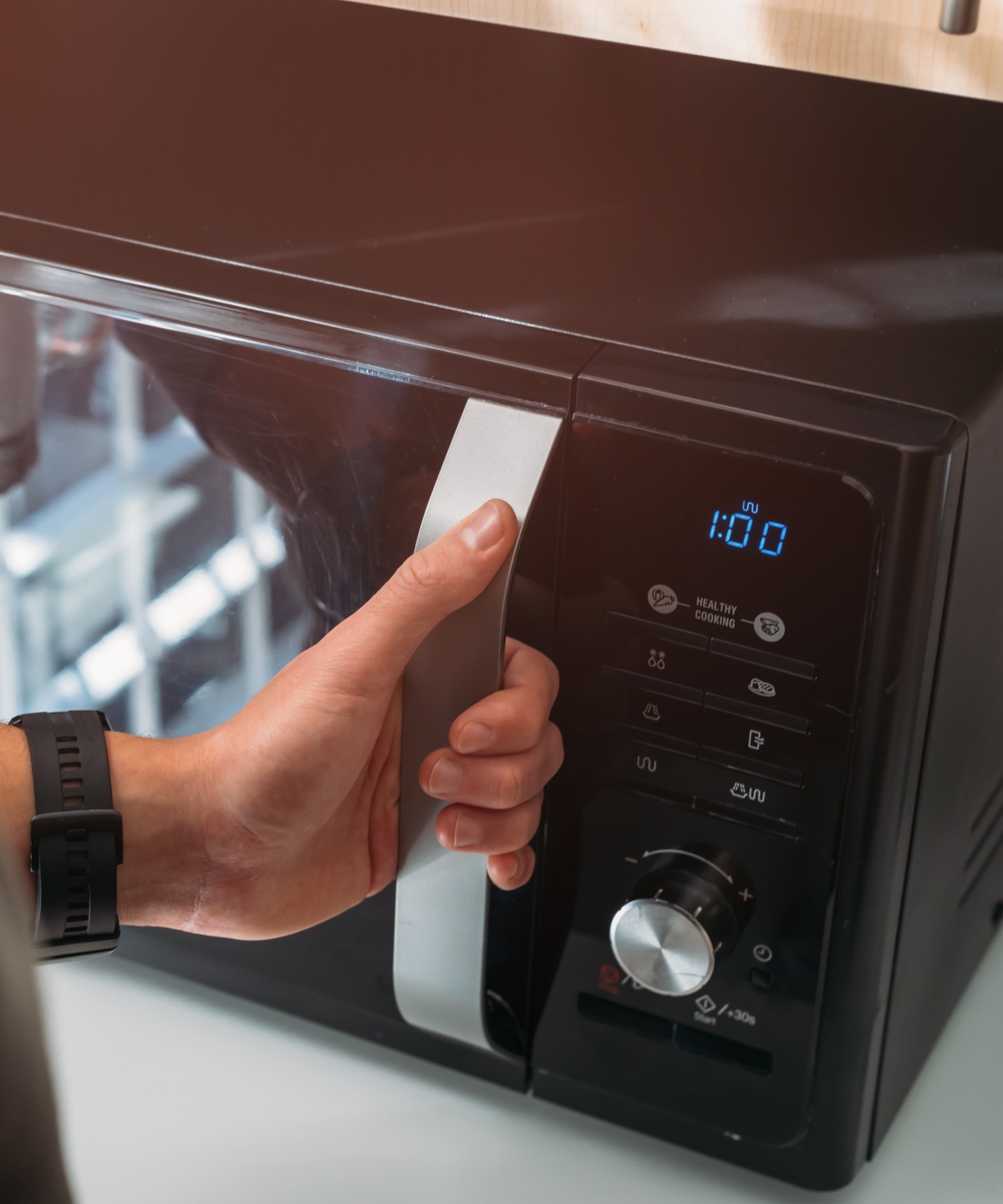 Eine Hand öffnet die Tür einer Mirkowelle.