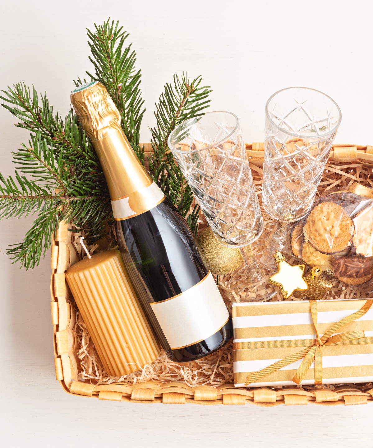 Geschenkkorb mit Sekt, Tannenzweigen, Keksen, Gläsern und goldenen Dekorationen.