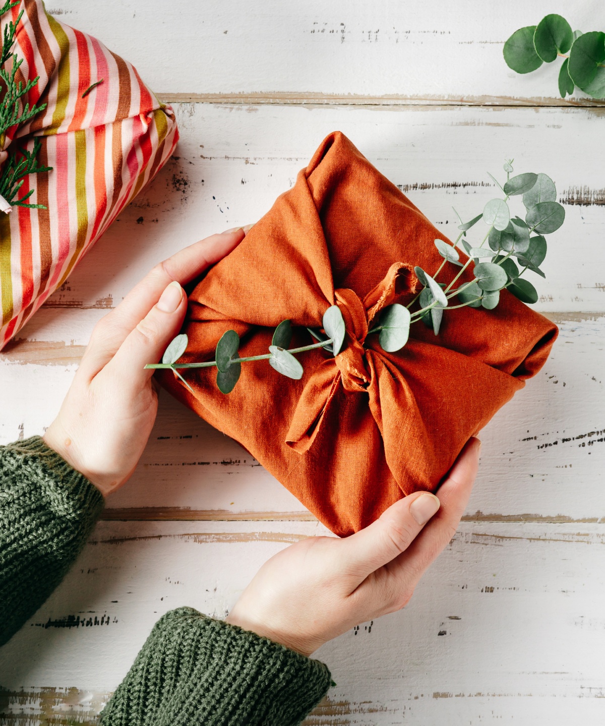 Zwei Geschenke in Stoff verpackt, dekoriert mit Zweigen und Eukalyptus.
