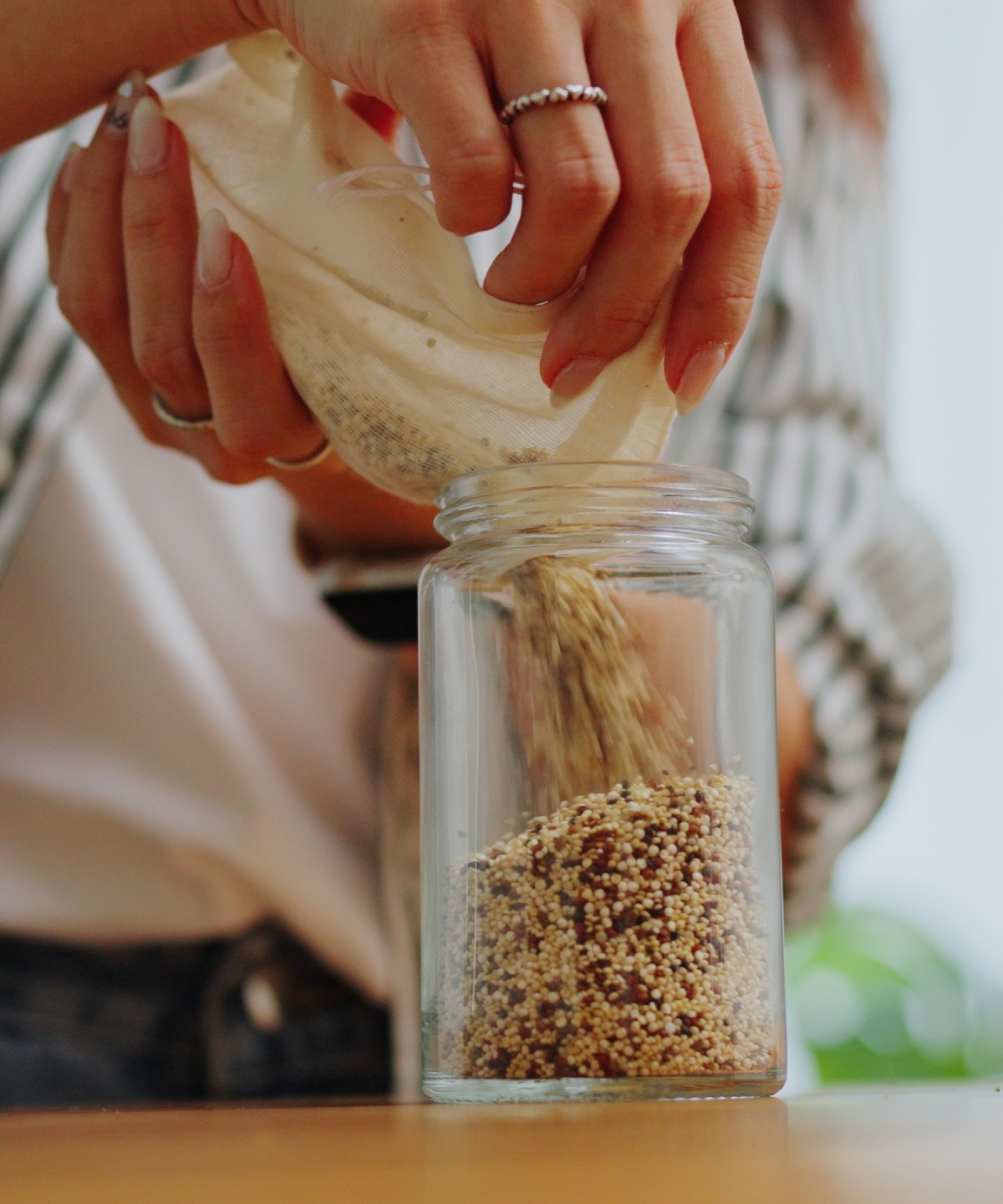 Nahaufnahme von Händen, die Quinoa aus einem Beutel in ein Glasgefäß füllen.