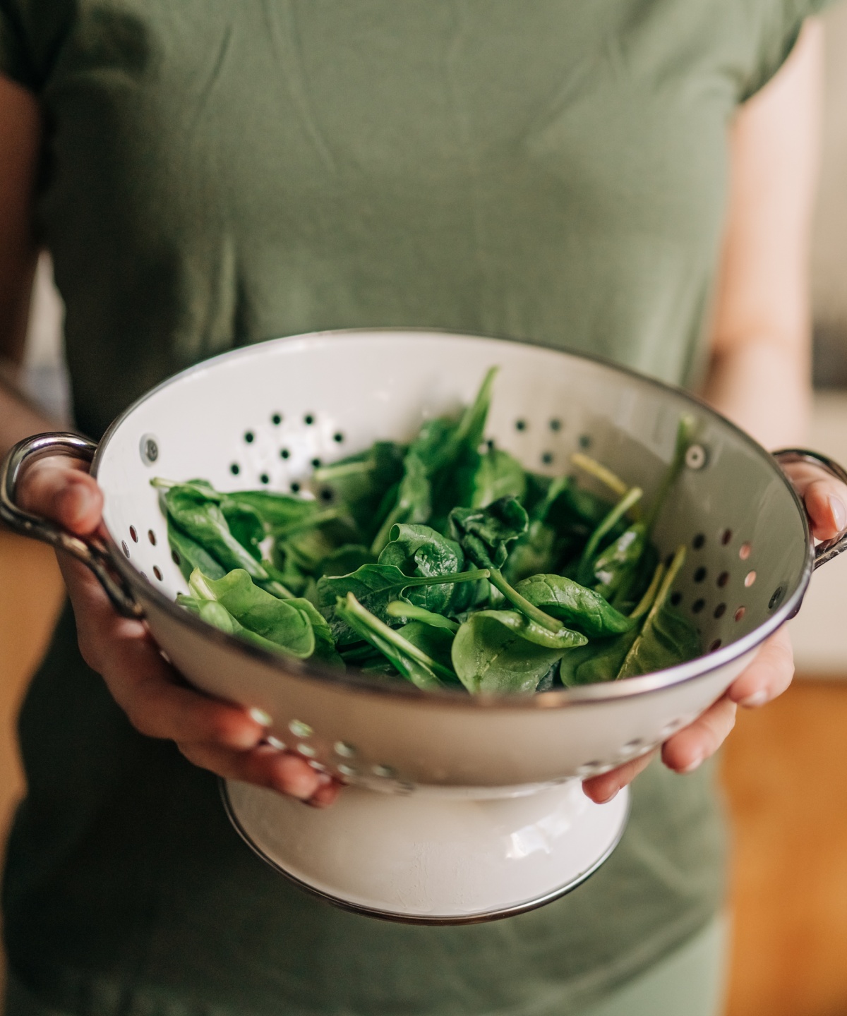 Frau hält ein Sieb mit frisch gewaschenem Spinat in den Händen.