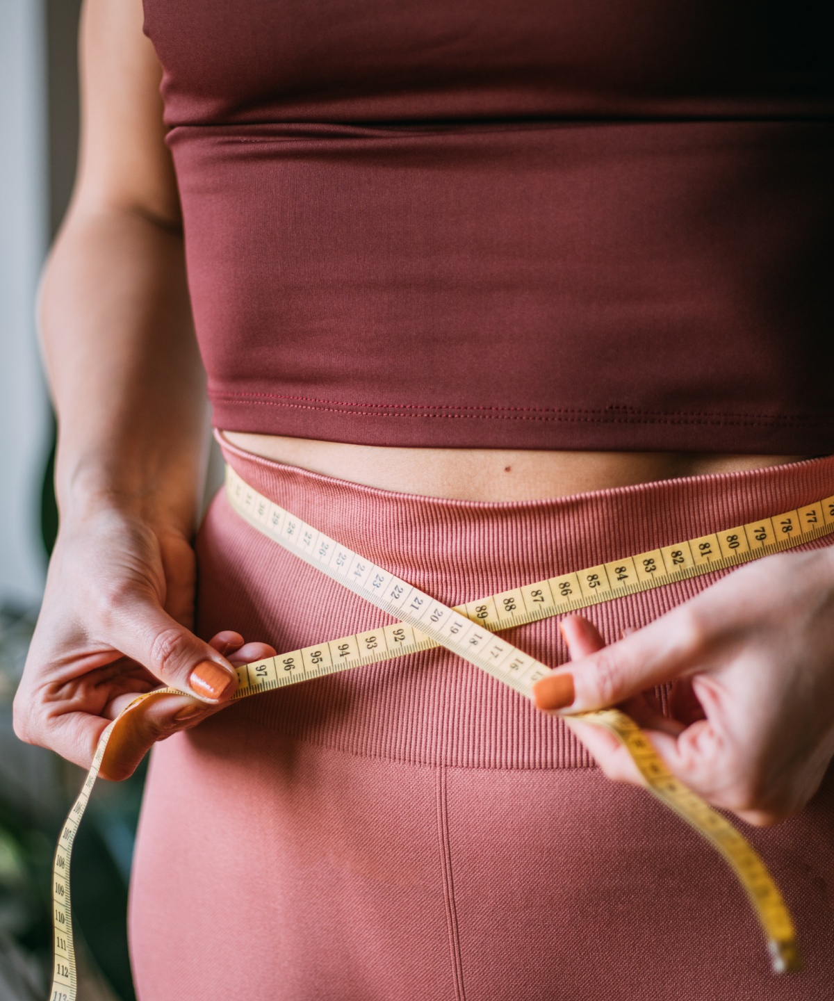 Frau in Sportkleidung misst mit einem Maßband ihren Taillenumfang.