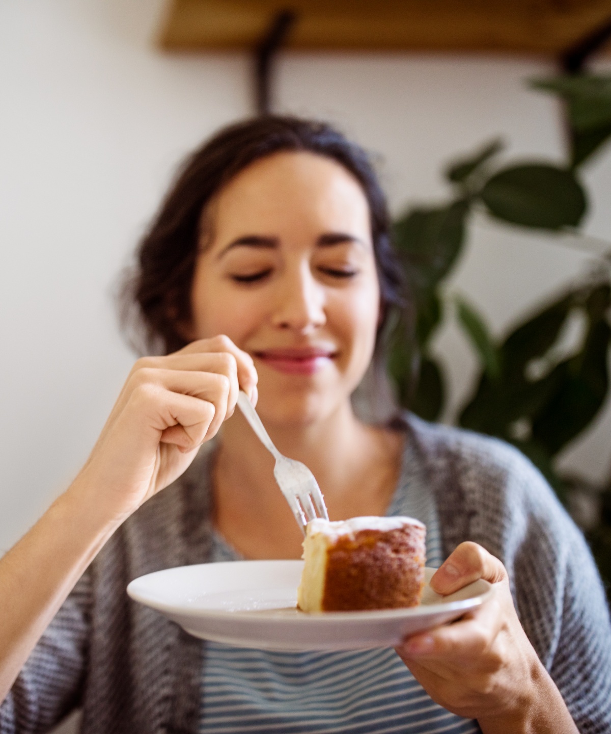 Frau genießt ein Stück Kuchen auf einem Teller mit einer Gabel.
