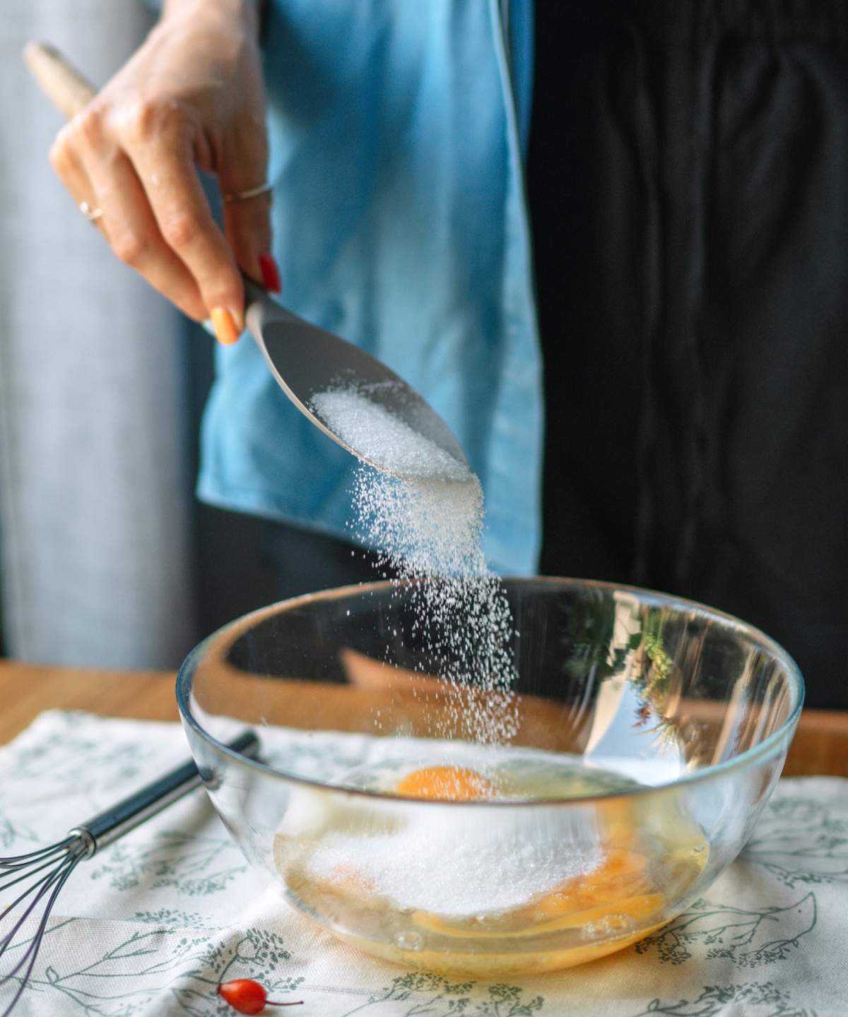 Person gibt Zucker in eine Schüssel mit Eiern, als Vorbereitung zum Backen.