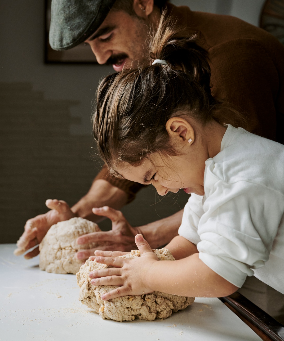 Vater und Tochter kneten gemeinsam Teig auf einem Tisch.