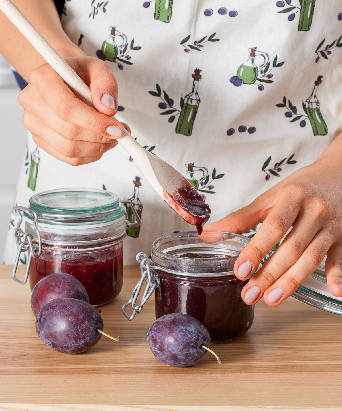 Person verschließt ein Glas mit Pflaumenmarmelade nach dem Einkochen im Backofen.