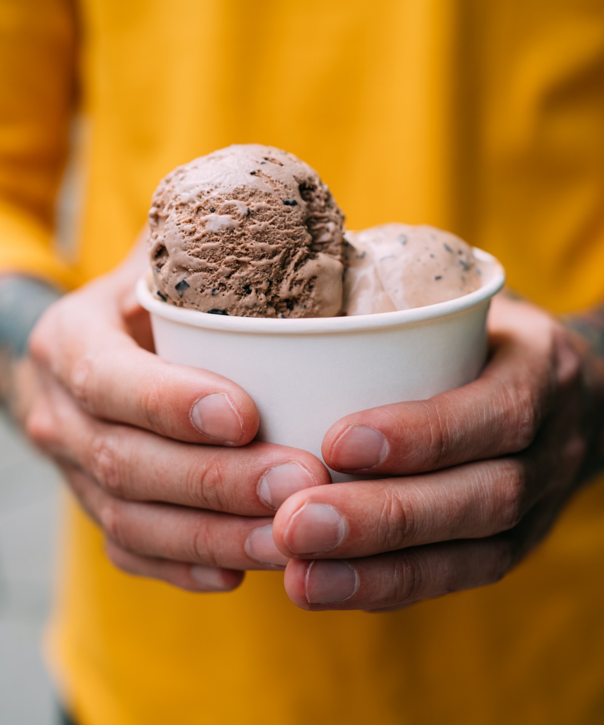 Eine Person in einem gelben Shirt hält einen Eisbecher in der Hand.