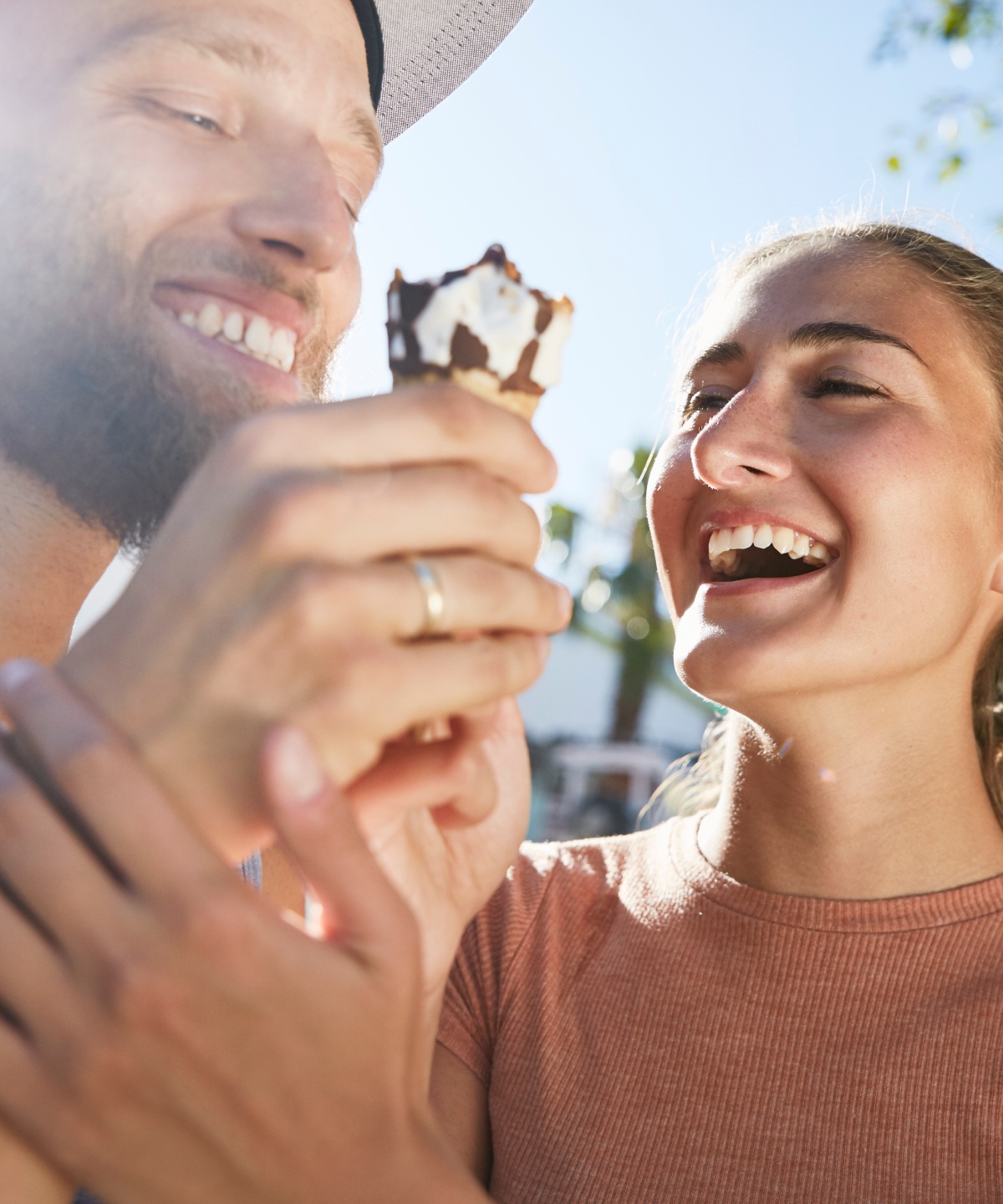 Lachendes Paar teilt sich ein Hörnchen-Eis bei Sonnenschein.