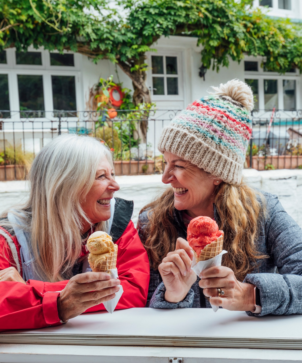 Zwei fröhliche Frauen genießen ein Eis in der Waffel bei kühleren Temperaturen.