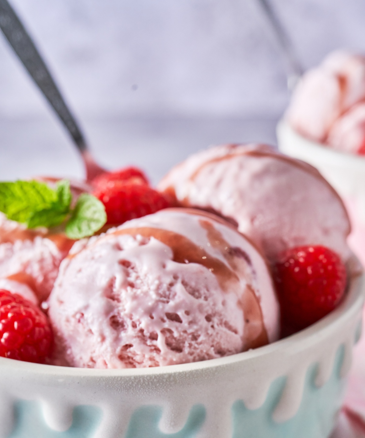 Drei Kugeln Erdbeereis in der Schale mit Sauce und Himbeeren und Minze garniert.