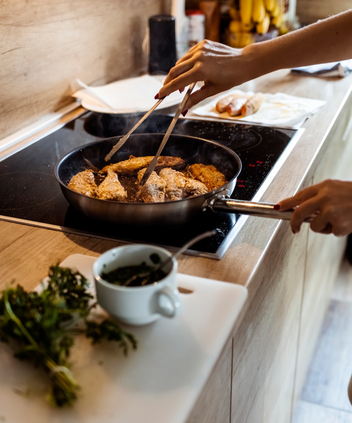 Eine Person brät in einer Pfanne Fisch an und wendet die Filets mit einer Zange.