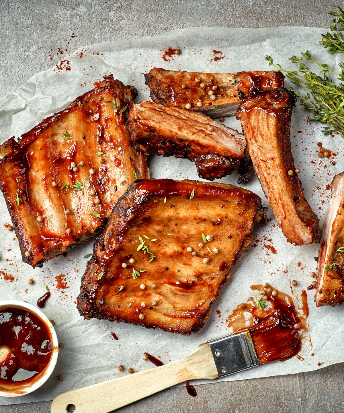 Marinierte Rippchen mit Thymianzweigen, Pinsel und der Marinade auf einem Stück Backpapier.