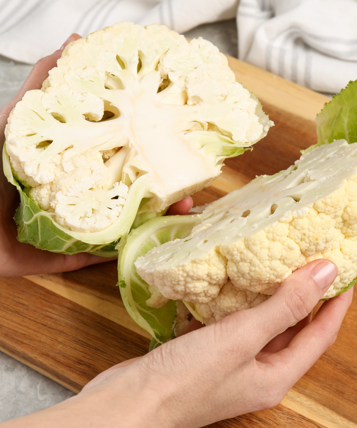 Zwei Hälften eines frischen Blumenkohls werden auf einem Schneidebrett für die Zubereitung vorbereitet.