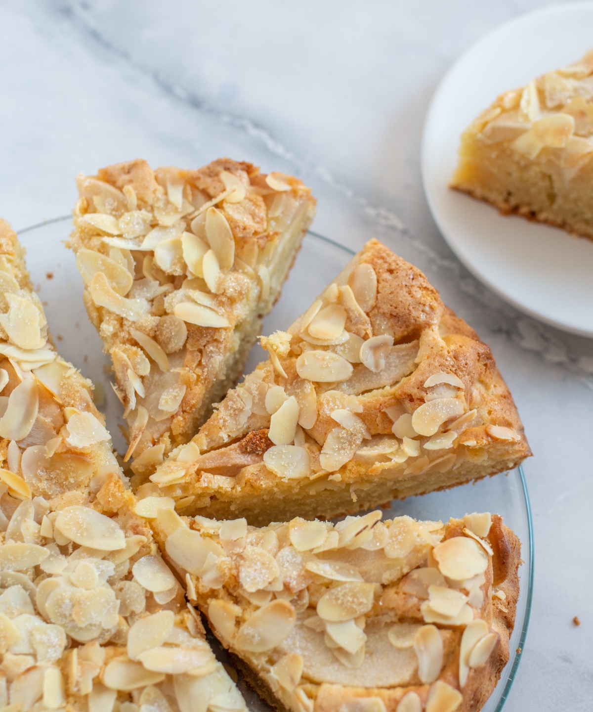 Ein saftiger glutenfreier Apfelkuchen mit Mandelblättchen, aufgeschnitten auf einem Glasteller.