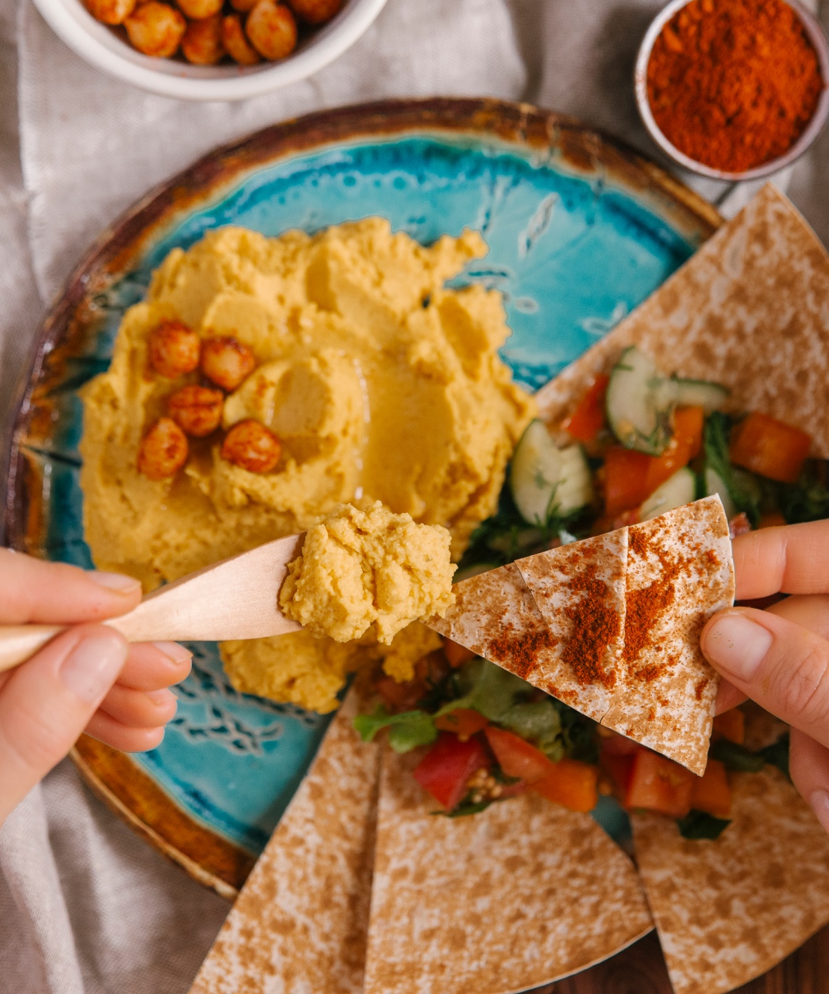 Mehrere Ecken Pitabrot liegen auf einem Teller mit griechischem Salat. Ein Stück Pita wird mit einer griechischen Paste bestrichen.