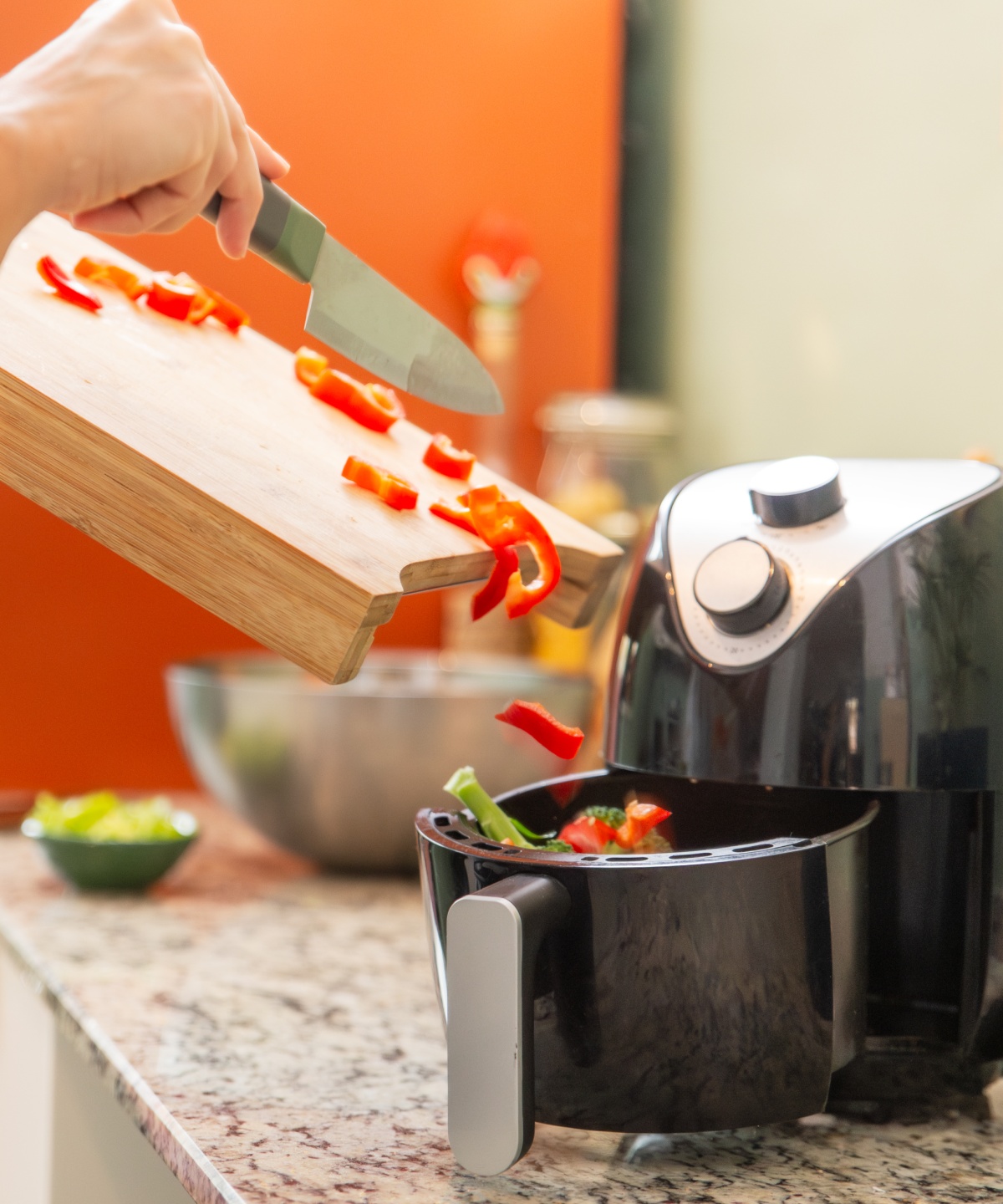 Eine Frau gibt geschnittene Paprika von einem Holzbrett in eine Heißluftfritteuse.