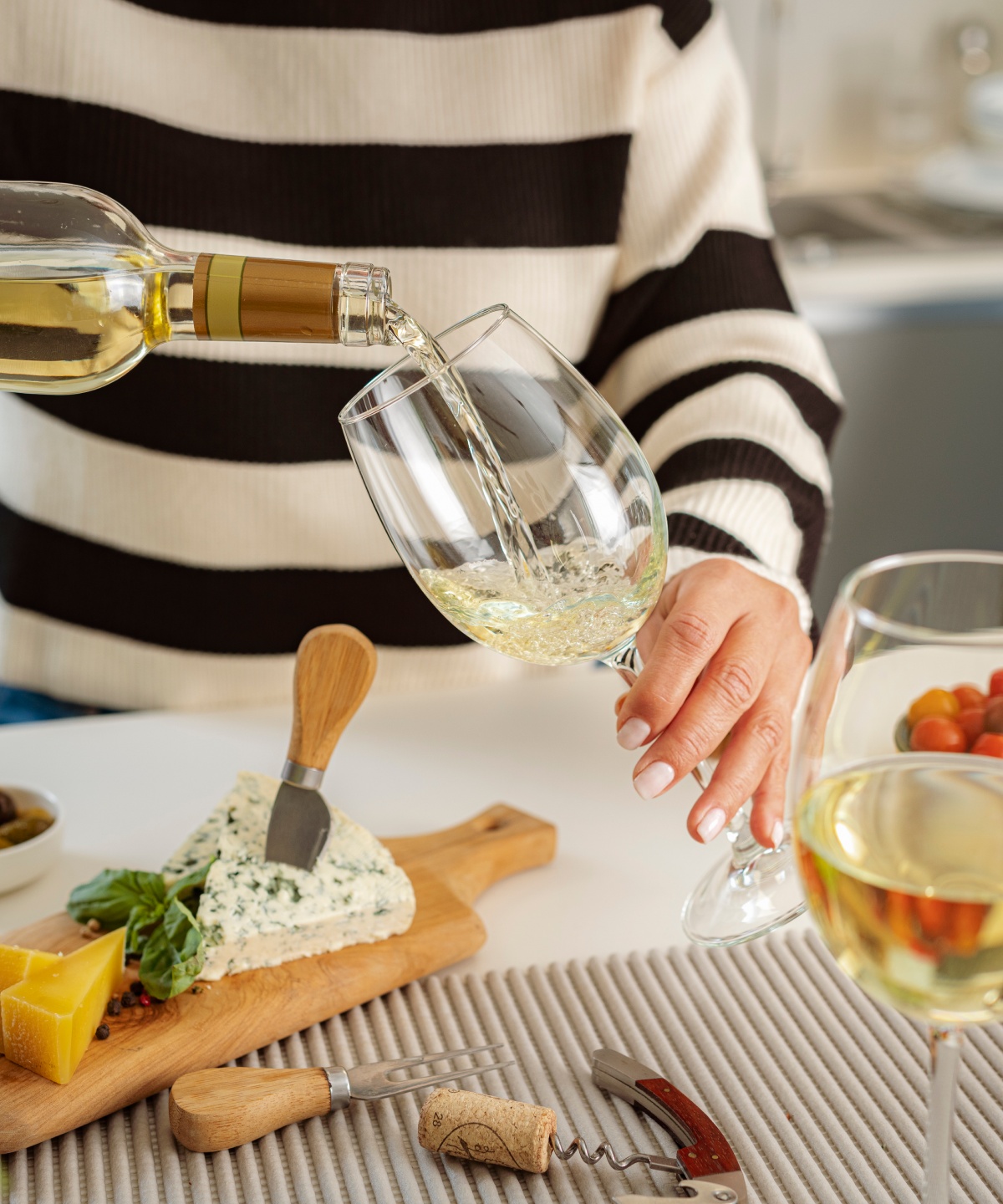 Eine Frau schenkt zu einer Käseplatte Weißwein in Gläser ein.