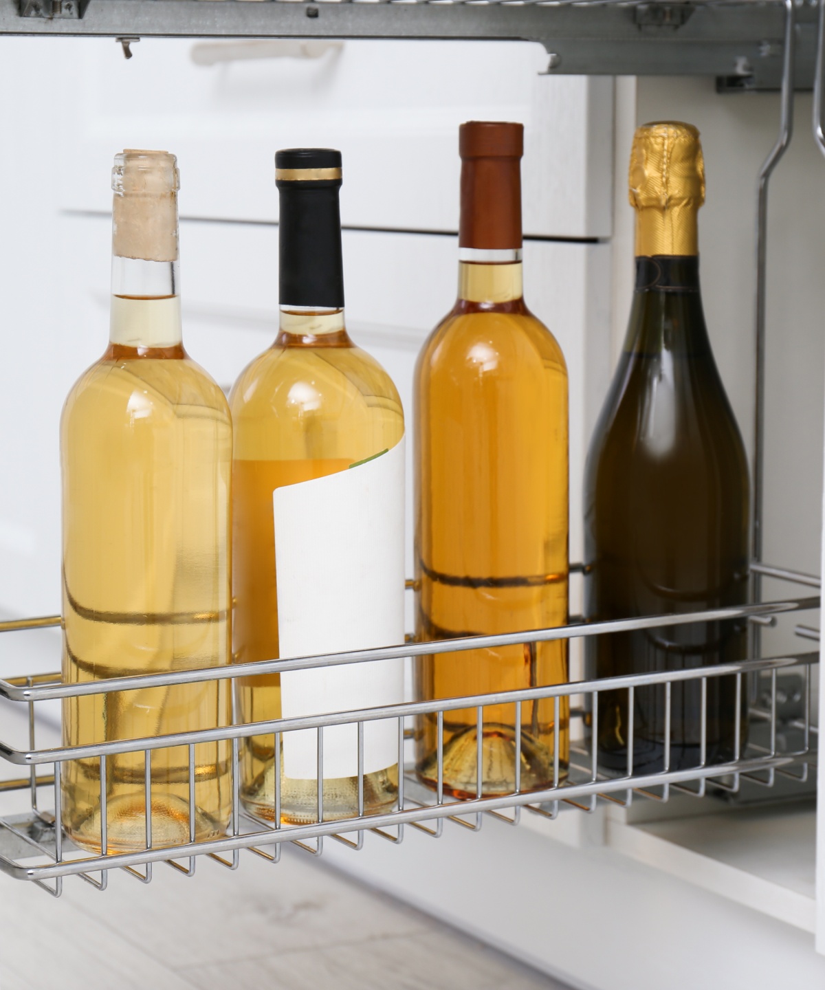 Vier Weinflaschen stehen in einem ausziehbaren Küchenregal.