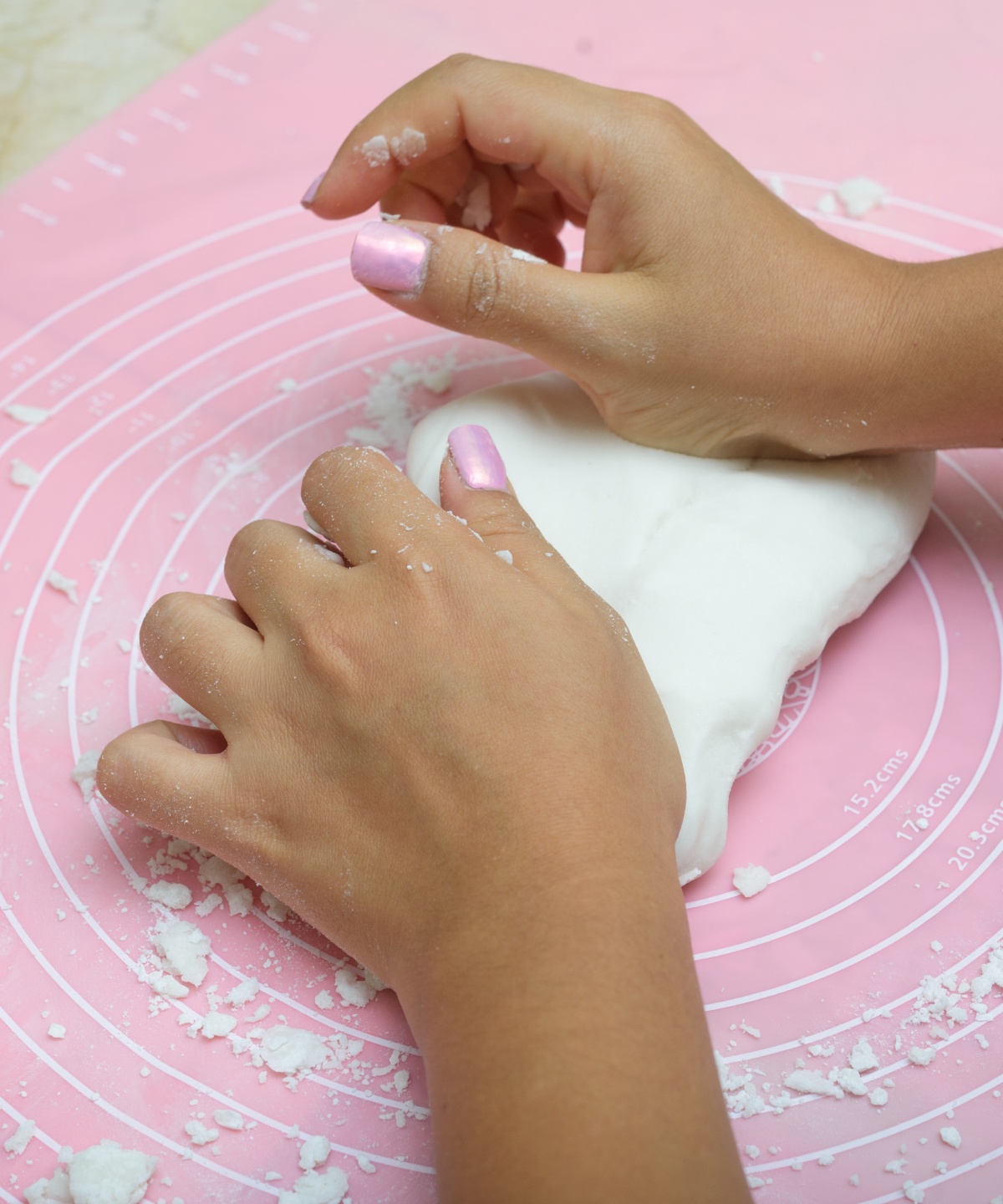 Jemand knetet mit den Händen einen weißen Teig auf einer rosa Backunterlage mit kreisförmigen Markierungen und Mehlresten.