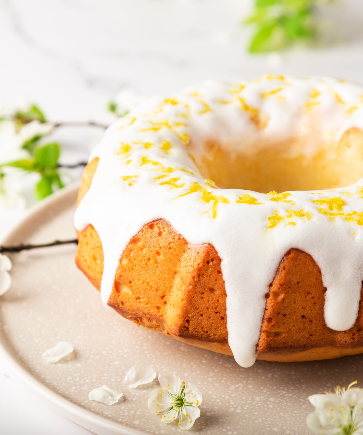 Zitronengugelhupf mit Zuckerguss und Zitronenzeste dekoriert auf einem Teller.
