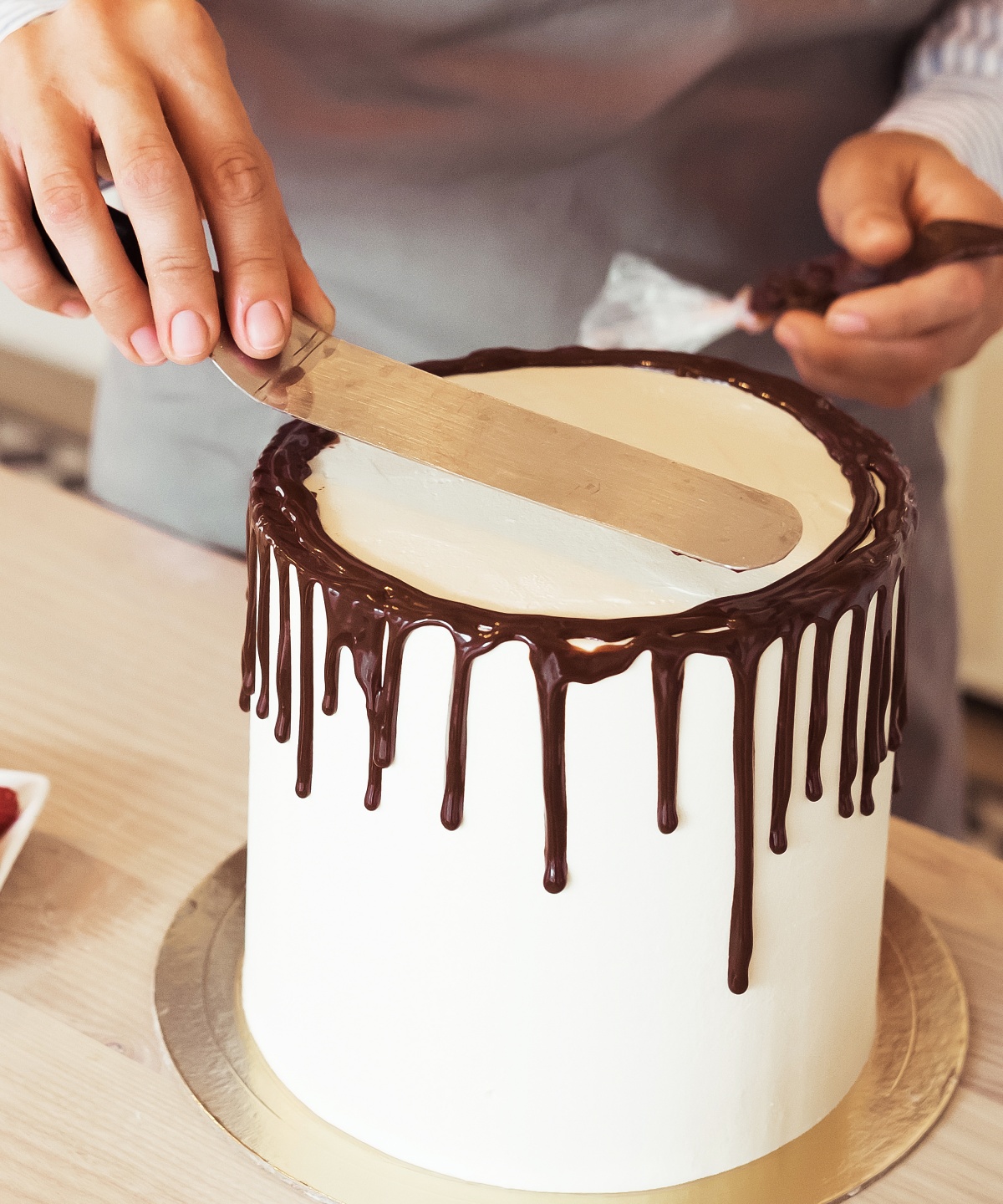 Konditor glättet weiße Torte mit am Tortenrand herabtropfender Schokoladenglasur.