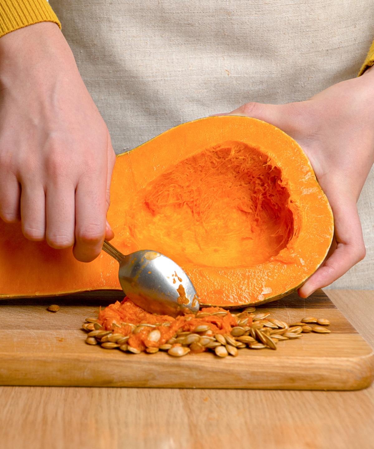Person höhlt mit einem Löffel einen halben Kürbis aus und entfernt Kerne und Fruchtfleisch.