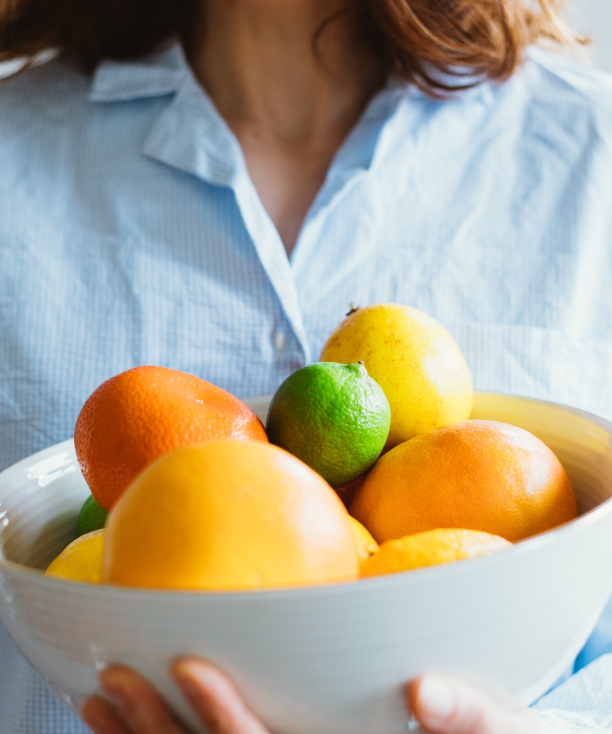 Person hält eine Schüssel mit bunten Zitrusfrüchten, darunter Orangen, Zitronen und Limetten.