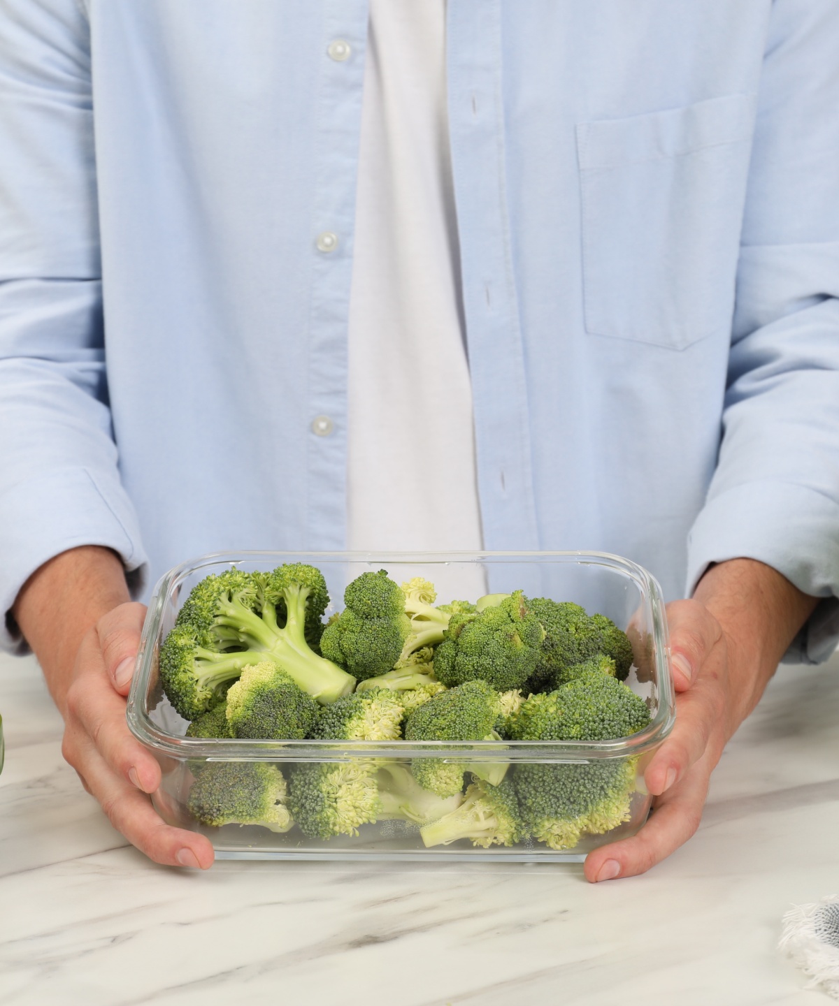 Person hält eine Frischhaltebox mit frischem Brokkoli, umgeben von weiteren Gemüsebehältern in der Küche.