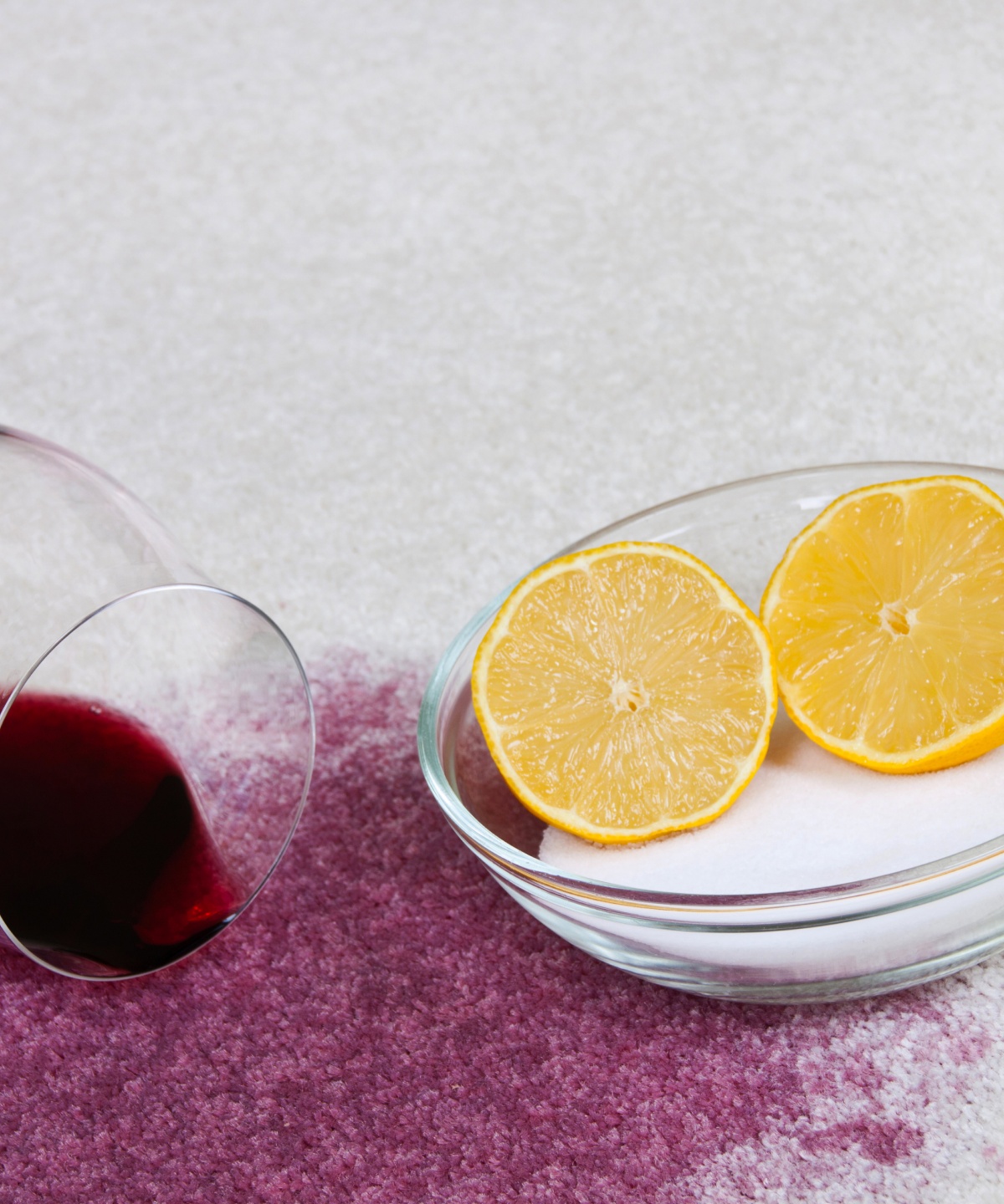 Ein Rotweinfleck breitet sich auf dem hellen Teppich aus. Daneben steht eine Schüssel mit Salz und Zitronensaft