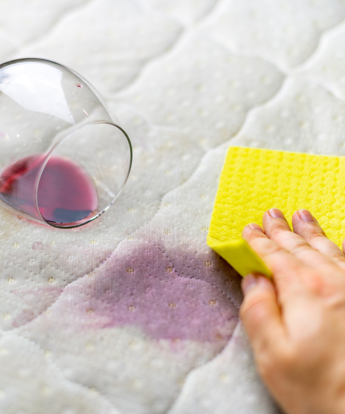 Eine Person tupft mit einem gelben Schwamm auf einen Rotweinfleck, der gerade einen hellen Stoff verfärbt