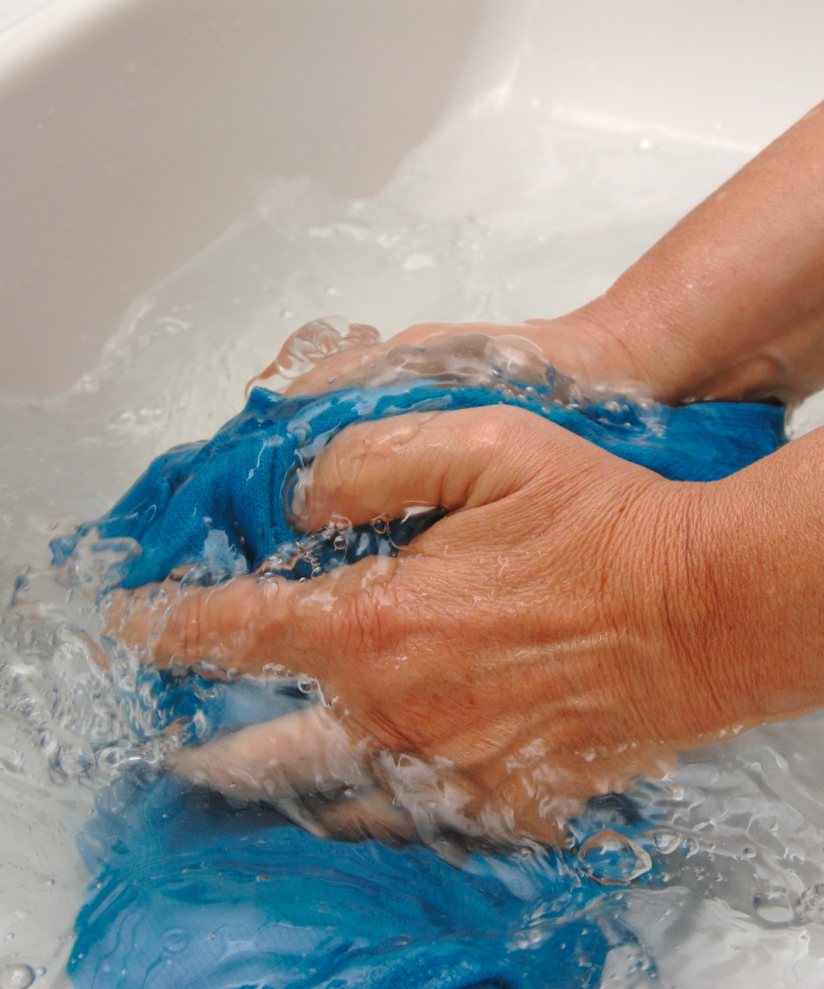 Eine Person wäscht ein blaues Kleidungsstück aus Wolle in einem Waschbecken mit klarem Wasser